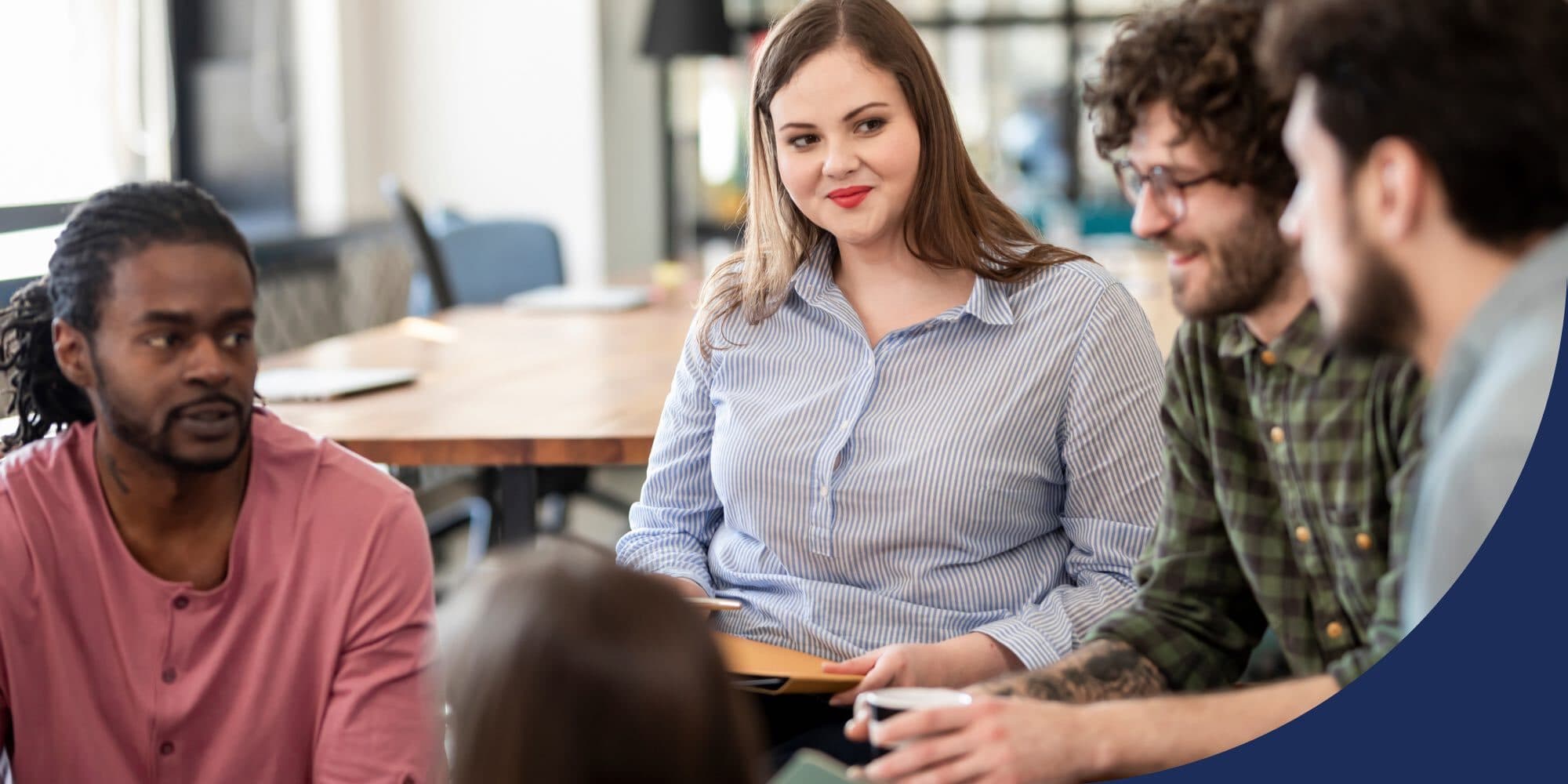 group of coworkers sitting huddled in an office talking, listening to one another, and smiling