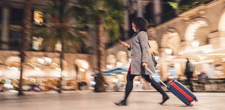 person looking at phone and pulling suitcase