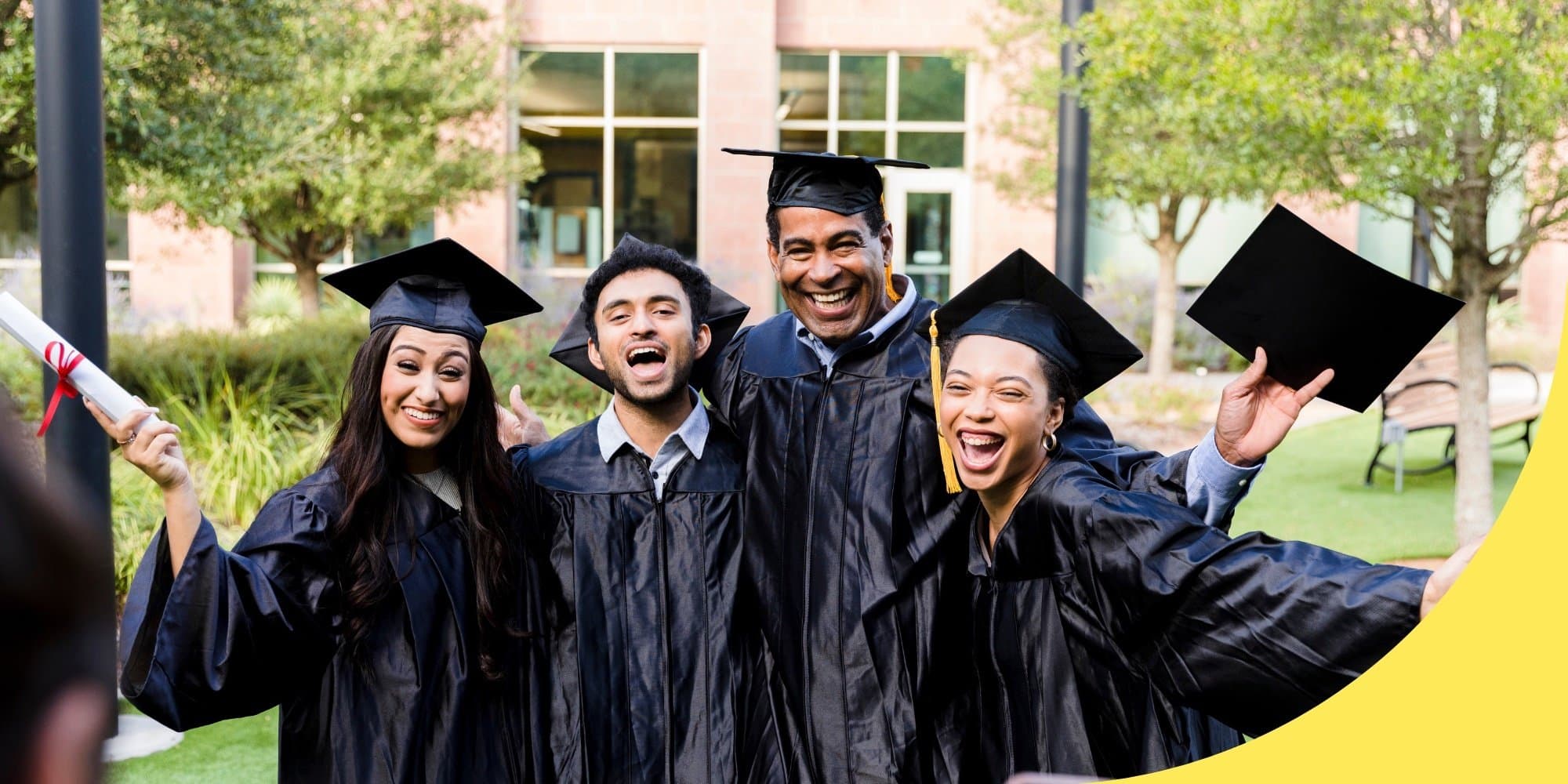 group of four graduates in black caps and gowns posing with their arms around one another for a picture