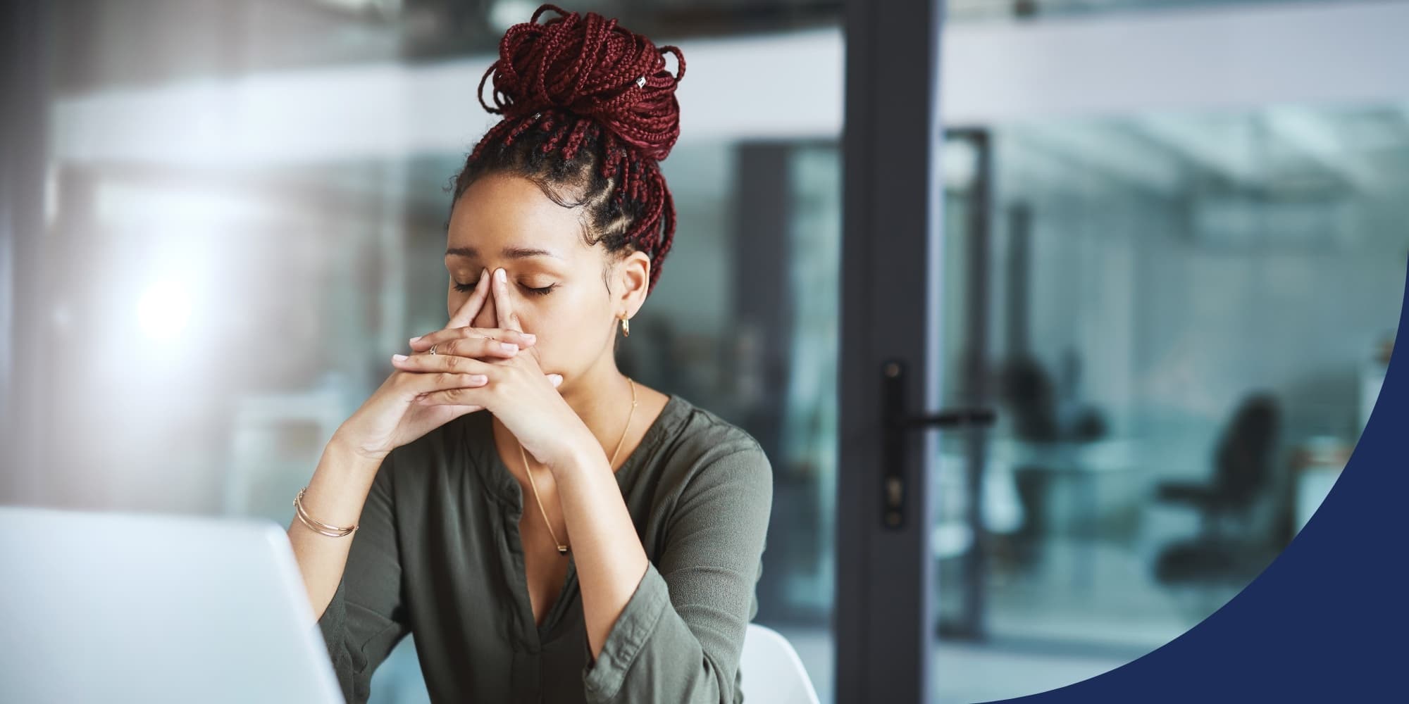 stressed person with hands on their face, sitting in an office conference room with glass walls