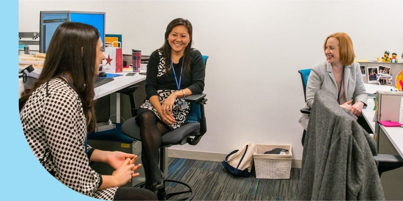Three coworkers chatting by their desks at an office